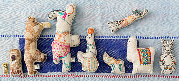 Coral and Tusk embroidered circus animals lined up on blue kantha quilt.