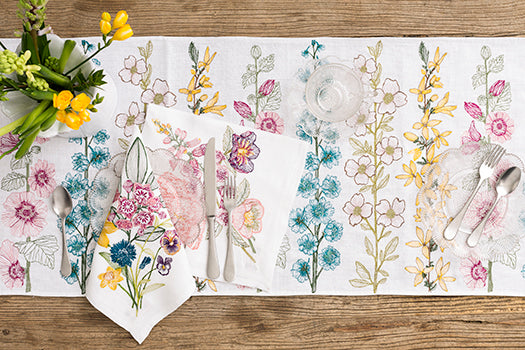 Overhead image of wood table with Coral and Tusk white floral embroidered table runner and dinner napkins.