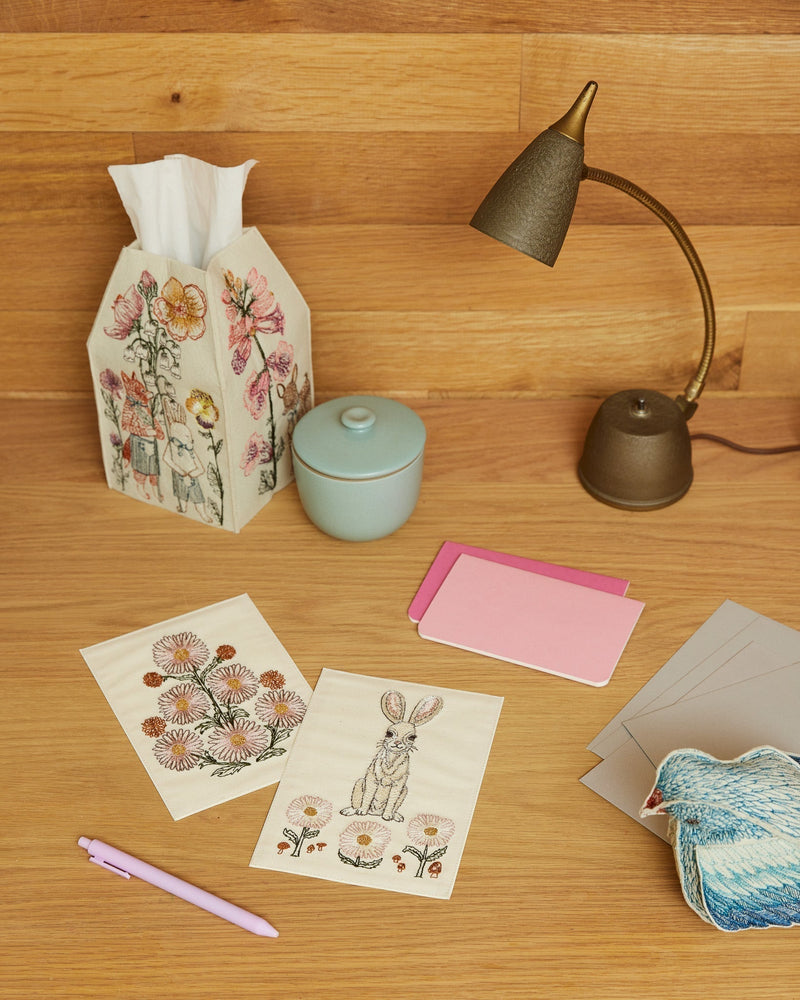 Coral & Tusk embroidered Spring Parade Tissue Box Cover on a wood desk with cards, bird and lamp