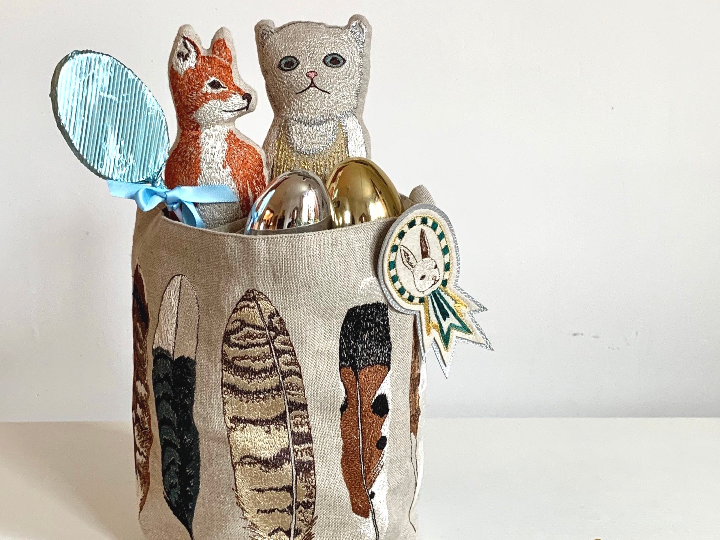 Coral & Tusk Embroidered feather bucket holding Easter eggs and Fox and Baby Cat pocket dolls