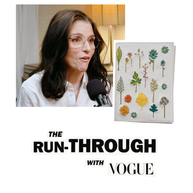 Julia Louis-Dreyfus speaking into a microphone during a video interview, beside a Coral & Tusk embroidered botanical notebook cover, over 