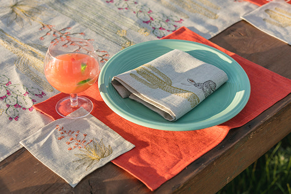 Coral and Tusk embroidered table linens with cactus motif table setting with table runner, orange placemat, napkin and orange drink.