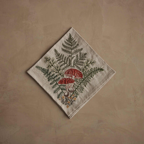 Coral & Tusk 20 × 20-inch folded embroidered linen Mushroom and Ferns Bouquet Dinner Napkin featuring a variety of ferns and mushrooms embroidered in green, rust, and marigold.