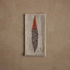 Coral & Tusk 20 × 20-inch folded embroidered linen Pheasant Feather Dinner Napkin featuring a pheasant feather embroidered in intricate brown and orange threads.