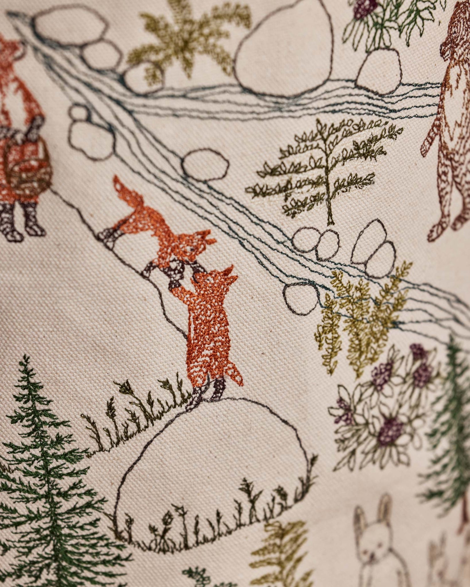 Close-up of the Coral & Tusk Forest Fun Bucket, a cylindrical fabric storage basket, showing detail of the fox family within an all-over embroidered woodland print of trees, deer, foxes, and a stream on an off-white canvas background.