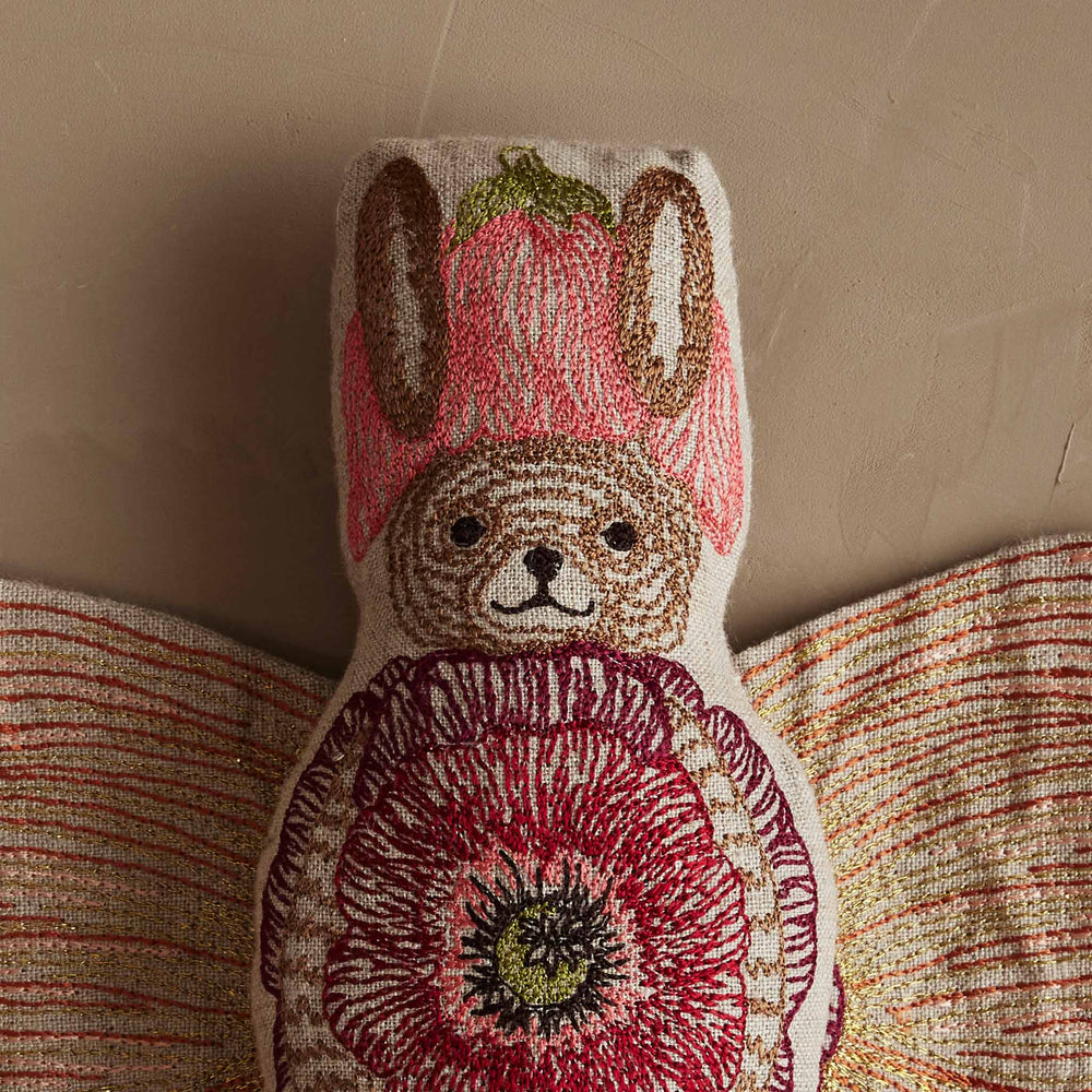 Close-up of Coral & Tusk embroidered Bunny Fairy Doll wearing a petal-shaped hat, with a smiling face and wings open to reveal an embroidered flower outfit.