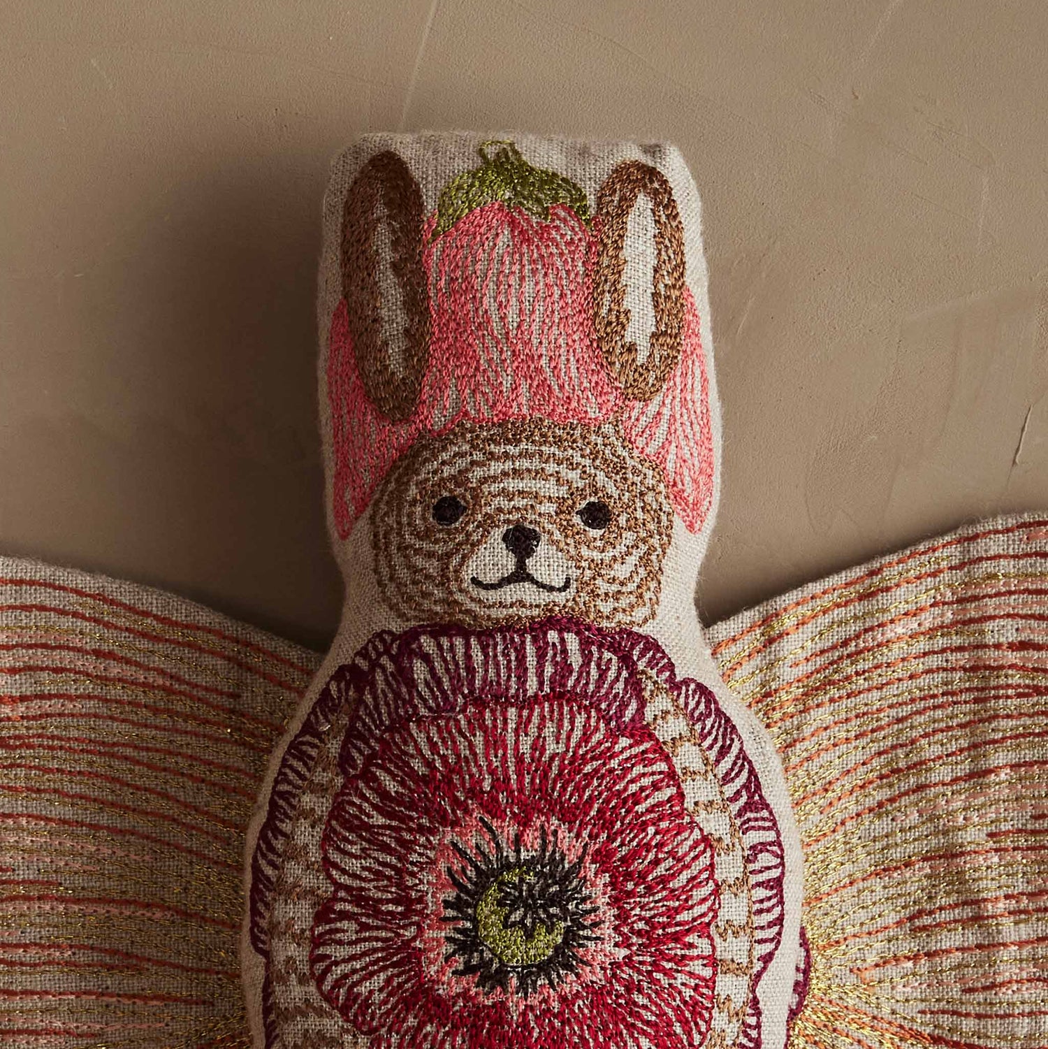 Close-up of Coral & Tusk embroidered Bunny Fairy Doll wearing a petal-shaped hat, with a smiling face and wings open to reveal an embroidered flower outfit.