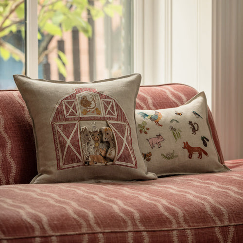 Two Coral & Tusk farm and garden-themed embroidered pillows styled on a red-striped sofa in front of a window with natural light.