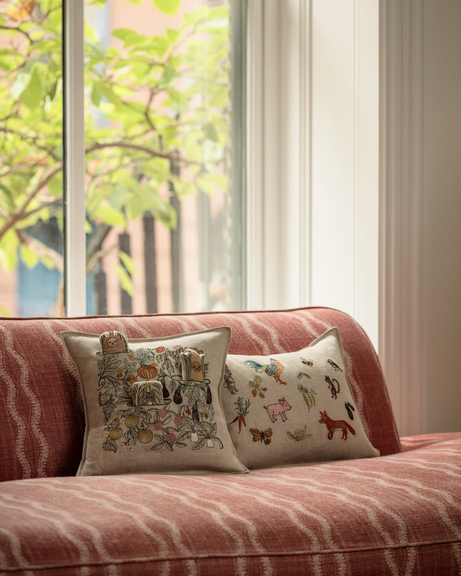 Coral & Tusk garden- and animal-themed embroidered decorative pillows on a red-striped sofa in front of a window with soft natural light.