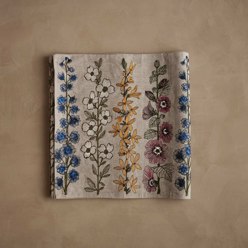 Coral & Tusk embroidered natural linen Spring Stems Table Runner featuring detailed delphinium stems, dogwood and forsythia branches, and freshly cut hollyhocks, creating a garden-inspired design.
